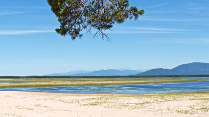 Fototapeta na wymiar Lakeshore panorama of mountain lake with pine branch and white sand