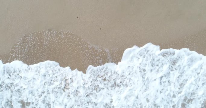 Static top down view of tropical beach, foamy ocean waves washing sand. Waves hitting sand beach