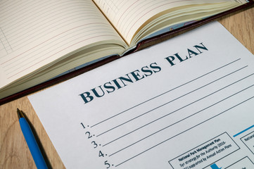 Business plan and pen on bright wooden office desk.