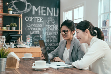 Two young asian female colleagues at coffee shop. businesswomen in suit using tablet computer with documents working in  morning in cafe. office ladies coworker taking break relaxing talking smiling.