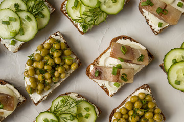 Hearty sandwiches of black bread with cucumbers, canned peas, salted fish on a gray background. Top view, close-up.