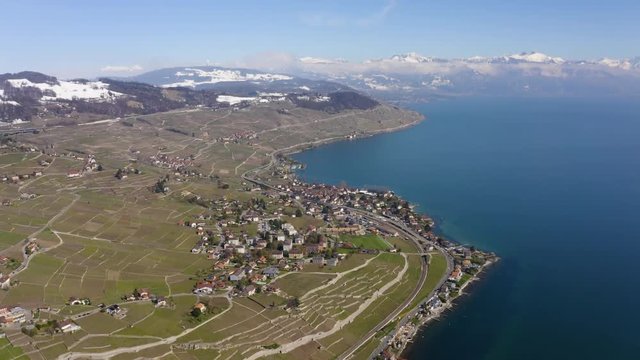 Aerial helicopter high shot over Grandvaux and Cully in Lavaux vineyard, spring season with snowy hills, Switzerland