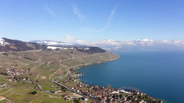 Aerial climb over Cully in Lavaux vineyard, spring season with snowy hills, Switzerland