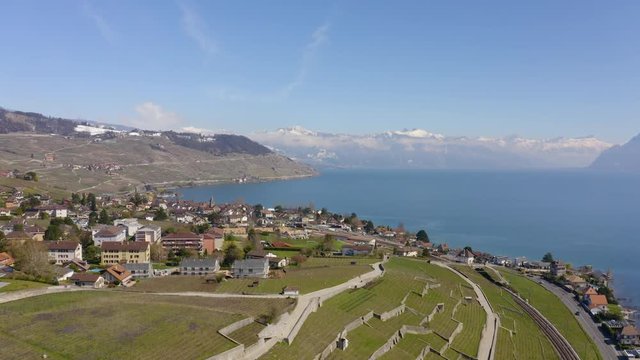Aerial reveal over Grandvaux and Cully in Lavaux vineyard, spring season with snowy hills, Switzerland