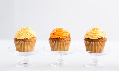 food, pastry and sweets concept - cupcakes with buttercream frosting on glass confectionery stand over white background