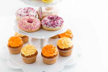 fast food and sweets concept - glazed donuts and cupcakes with buttercream frosting on stand over white background