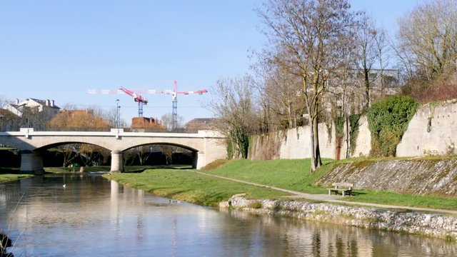 View on the meurthe river, in Nancy, north east France. In the forground, there is the river bank and in the background, we can see a bridge and a few cranes. Reflection on the water, blue sky.