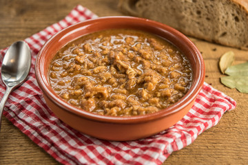 tripe stew sauce in brown ceramic pot on a wood table 