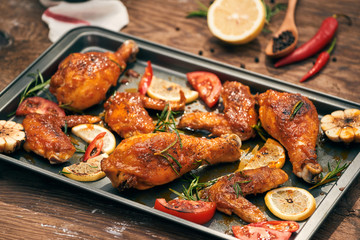 Baked chicken drumstick and wings on baking tray over dark wooden background.