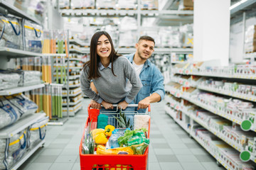 Couple with cart full of goods in a supermarket