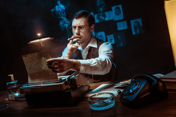 Detective in glasses smoking cigar while using typewriter in dark office