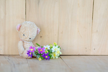 Teddy Bear Sit on a wooden floor and bouquet of flowers.