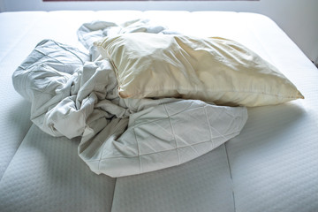 White crumpled bed sheet, Ivory pillow on white bed, Close up shot, Selective focus, Bedroom cleaning concept