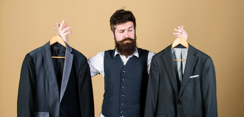 Doubting about his choice. Bearded man holding suit jackets in store, choice concept. Hipster...