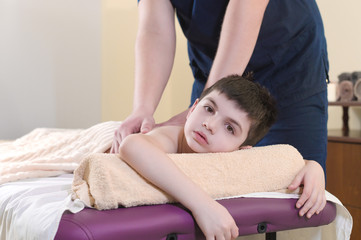 A little boy relaxes from a therapeutic massage. Male massage therapist makes a medical massage to the back of a child