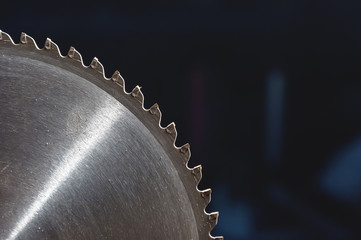 A closeup of a circular saw blade on a dark blue background. Shop for the production of wooden...