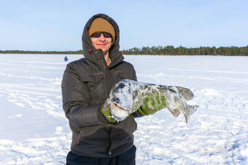 young man holding fish catch a big pike ice fishing