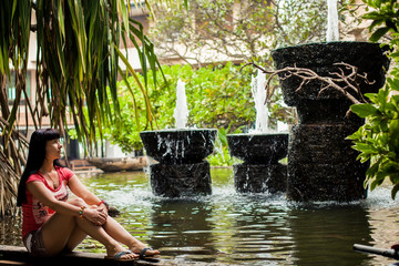 girl sitting in an exotic Park among the fountains. Travel concept. Back view. woman looking at waterfall in the hotel