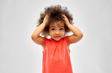 childhood and people concept - overwhelmed little african american girl holding to head over grey...