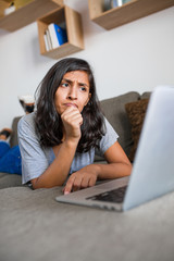 Young indian woman thinking in front of computer at home