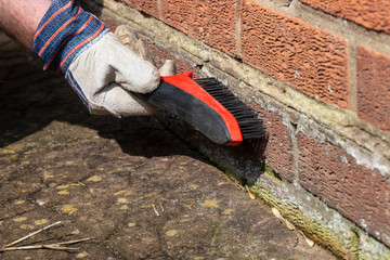 Man rubbing down brick wall with house removing water stain damage wearing gloves