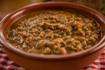 tripe stew sauce in brown ceramic pot on a wood table 