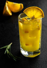 glass orange juice with ice and slices orange with rosemary branch on black background