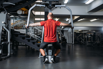 Fototapeta na wymiar Muscular athlete on exercise machine, back view