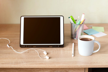 Wooden Desk. White tablet with black-rimmed glasses. Cup of tea.