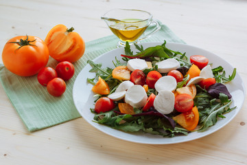 Fresh salad with arugula, cherry tomatoes, mozzarella cheese and olive oil on white wooden background