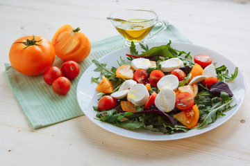 Fresh salad with arugula, cherry tomatoes, mozzarella cheese and olive oil on white wooden background
