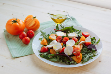 Fresh salad with arugula, cherry tomatoes, mozzarella cheese and olive oil on white wooden background