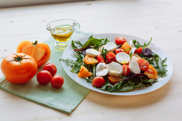 Fresh salad with arugula, cherry tomatoes, mozzarella cheese and olive oil on white wooden background