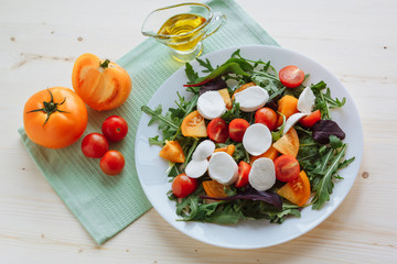 Fresh salad with arugula, cherry tomatoes, mozzarella cheese and olive oil on white wooden background