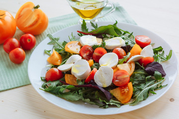 Fresh salad with arugula, cherry tomatoes, mozzarella cheese and olive oil on white wooden background
