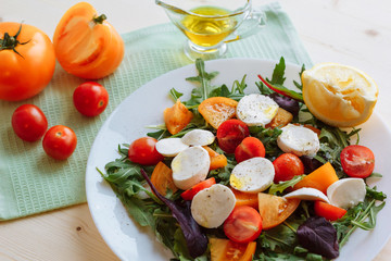 Fresh salad with arugula, cherry tomatoes, mozzarella cheese and olive oil on white wooden background