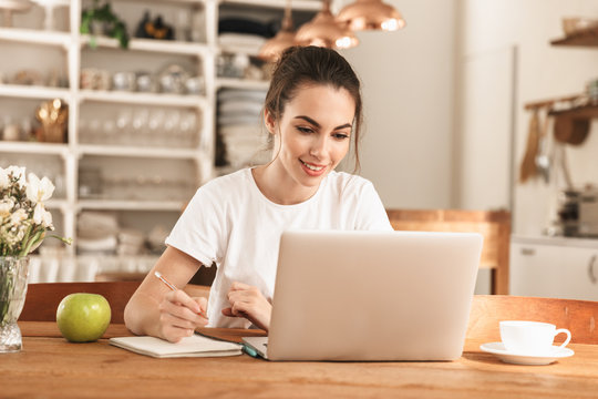 Beautiful young student girl with apple indoors using laptop computer.
