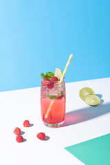 iced red raspberry punch cocktail with lime in glass on color background. summer drink.