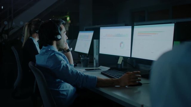 Late at Night In Modern Office: Row of 24/7 Support People and Salesmen Working at their on Desktop Computers, Using Headsets and Making Calls, Talking to Clients and Customers