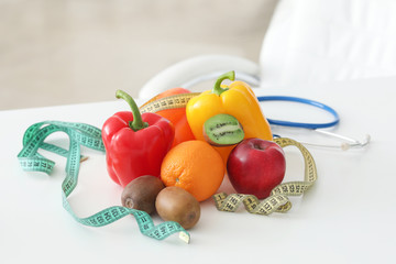Fresh fruits and vegetables with measuring tapes on table of nutritionist in office