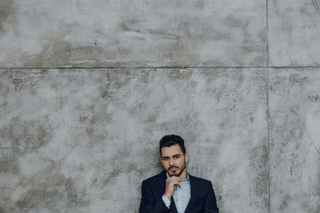 Thoughtful elegant male employee against grey wall