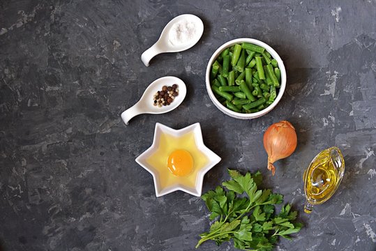 Ingredients for cooking green asparagus beans with scramble egg: raw green asparagus beans, egg, onion, salt, pepper, parsley, oil. Georgian cuisine. Top view, copy space.