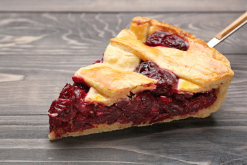 Piece of tasty cherry pie on wooden background