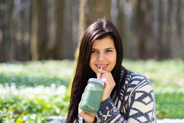Happy healthy eating girl drinking green smoothie detox outdoors in the wood. Woman on weight loss diet vegan nutrition cleanse.