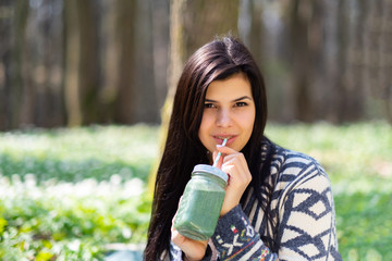 Happy healthy eating girl drinking green smoothie detox outdoors in the wood. Woman on weight loss diet vegan nutrition cleanse.