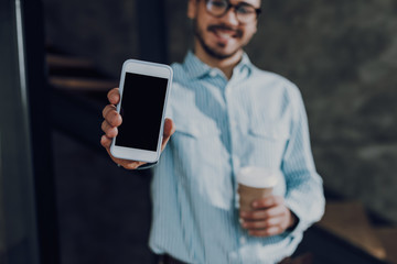 Cheerful guy with hot drink is demonstrating smartphone