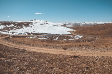 Landscape view of a winding dirt road along snow capped mountain range at Deosai Plain National Park, Astore. Gilgit Baltistan. Pakistan.