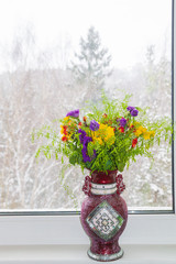 A beautiful vase of spring flowers stands on a window in a snowstorm