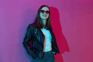 Fashioned girl in leather jacket in dark glasses in pink anf blue  neon lights background. 