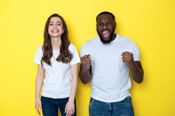Surprised lucky interracial couple in white T-shirts posing for camera in studio